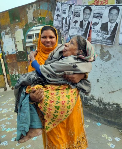বৃদ্ধা সাহেরা বেগমকে কোলে করে কেন্দ্রে নিয়ে এসেছেন তার বৌমা। ছবি: ইত্তেফাক