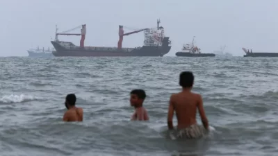 হরমুজ প্রণালিতে নোঙর করে আছে জাহাজ, পাশেই সাগরে সাঁতার কাটছে শিশুরা